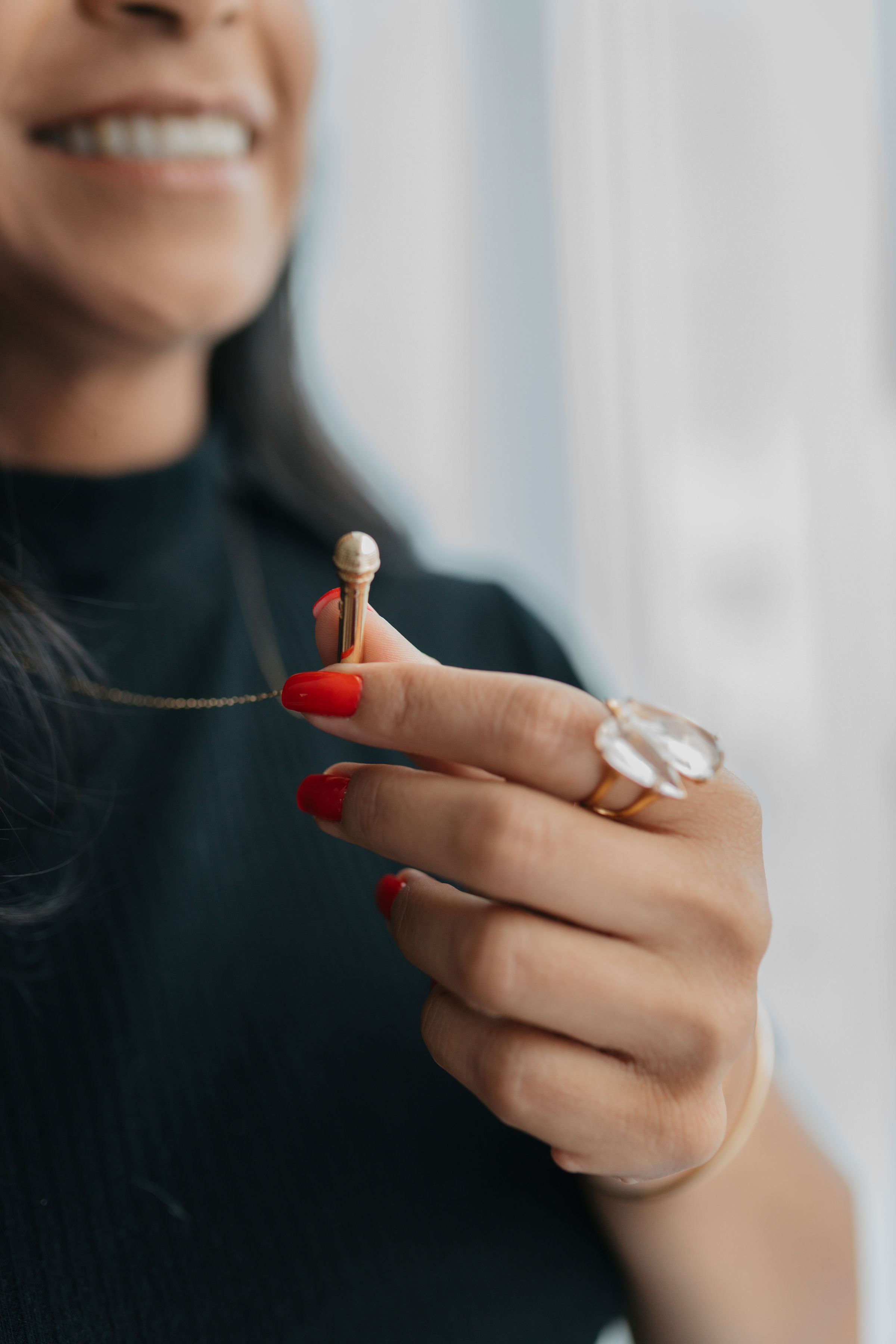 Close de Ana Lígia sorrindo segurando caneta, unhas vermelhas